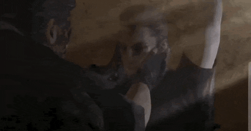 two men are standing next to each other in a dark room and looking at each other .