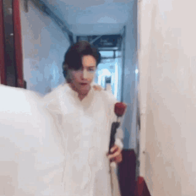 a man in a white shirt is holding a red rose and walking down a hallway .