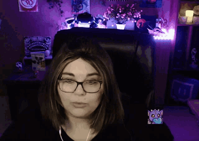 a woman wearing glasses sits in a chair with a purple background