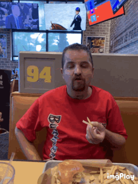 a man wearing a red budweiser shirt is eating french fries