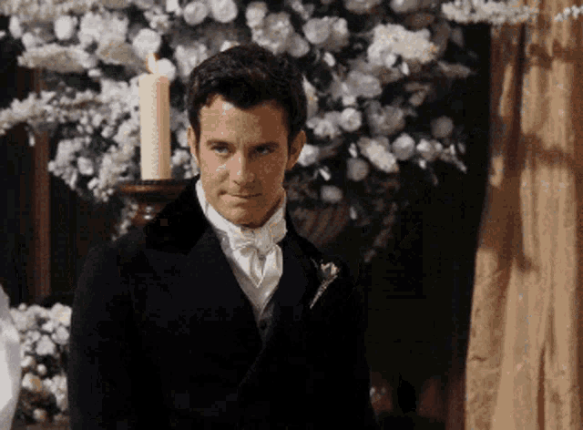 a man in a suit stands in front of a candle holder with flowers in the background