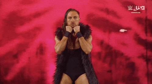 a wrestler with long hair is wearing a fur coat and a black bodysuit .