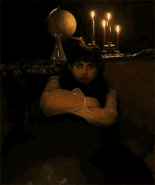 a woman is sitting on a couch in a dark room with candles and a globe .
