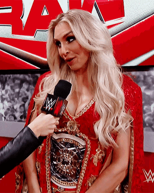 a woman in a red dress is being interviewed by a person holding a microphone that says raw on it