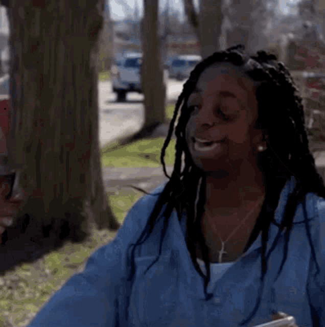 a woman with dreadlocks is smiling and holding a cell phone in her hand .