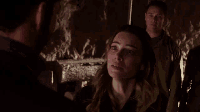 a man and woman are kissing in a dark room with a man in the background