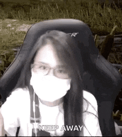 a woman wearing a mask and glasses is sitting in a chair and says `` keep away '' .