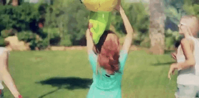 a girl is holding a balloon over her head while playing with other children in a park .