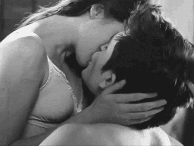 a black and white photo of a woman kissing a man on the neck .