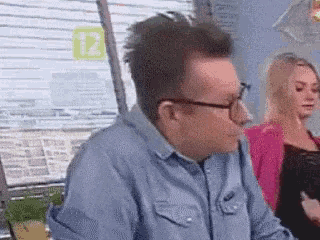 a man wearing glasses is sitting at a table with a woman in a pink jacket behind him .