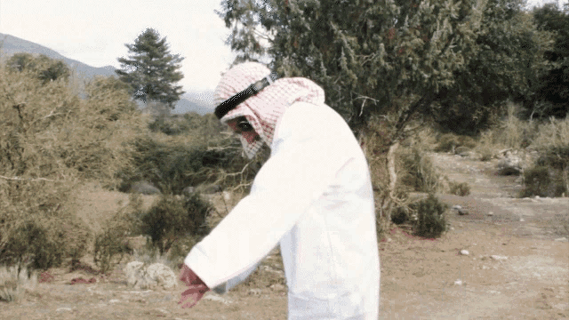 a man in a white robe and head scarf is standing in the dirt
