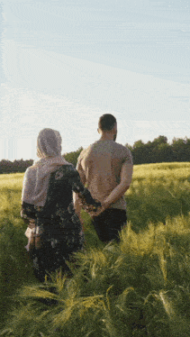 a man and a woman are holding hands while walking through a wheat field .