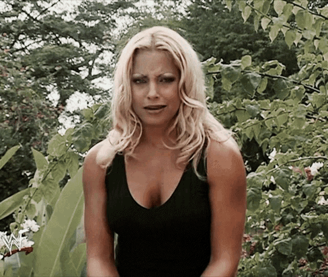 a woman in a black tank top stands in front of a tree with a wwe logo on it