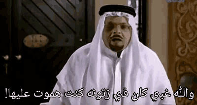 a man in a white robe is standing in front of a door and talking in arabic .