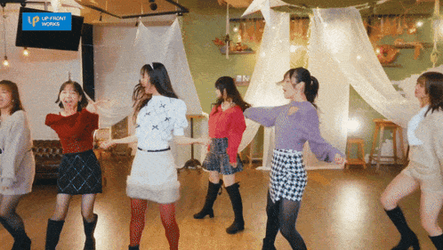 a group of young women are dancing in front of a sign that says up front works