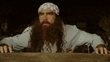a man with long hair and a beard wears a bandana and a white shirt