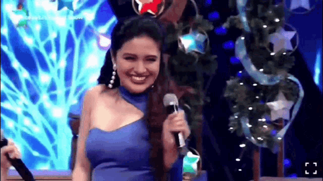 a woman in a blue dress is smiling while holding a microphone on a stage .