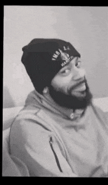 a black and white photo of a man with a beard wearing a beanie and a hoodie .
