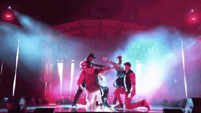 a group of people are dancing on a stage in front of a pink and blue light .