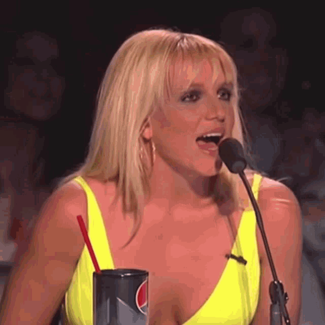 a woman in a neon yellow top is speaking into a microphone while holding a pepsi can