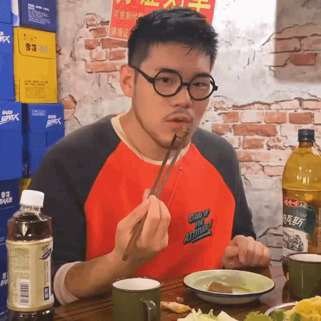 a man wearing a red shirt that says stand up for attitude is eating food with chopsticks