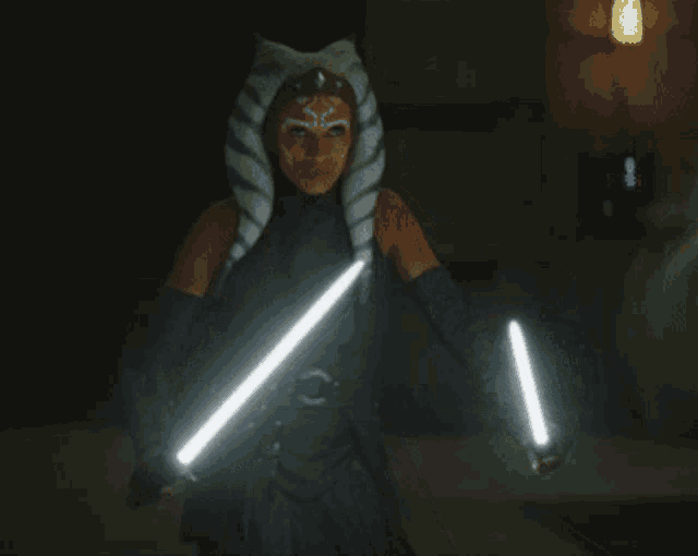 a woman in a costume holding two lightsabers in her hands