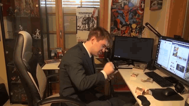 a man in a suit sits at a desk with a metal gear solid poster on the wall behind him
