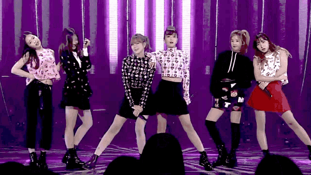 a group of girls are performing on a stage with purple lights