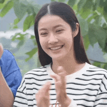 a woman in a striped shirt is clapping her hands and smiling .