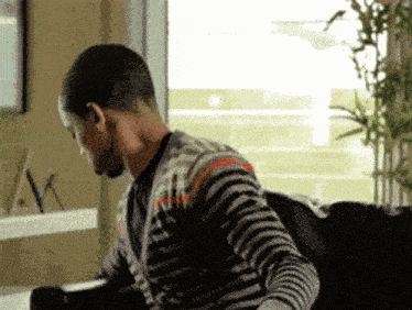 a man in a striped sweater is sitting on a couch in front of a window