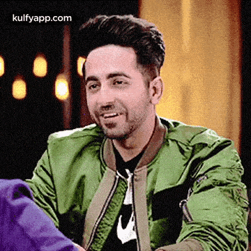 a man wearing a green jacket is smiling while sitting down .
