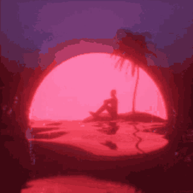 a person is sitting on a beach in front of a large red sun