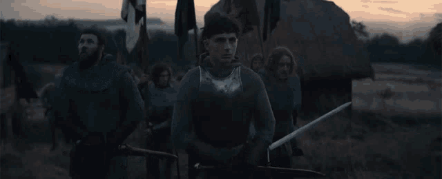 a man in armor is holding a sword in front of a group of men .