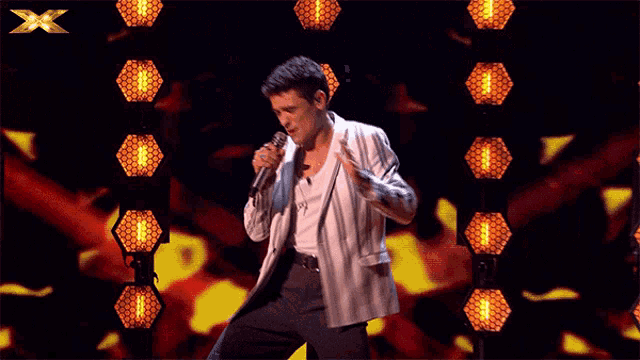 a man singing into a microphone on a stage with a x in the background