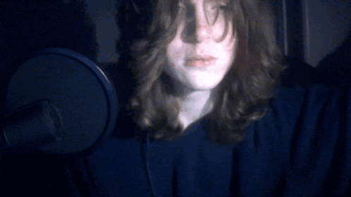 a woman with long hair stands in front of a microphone in a dark room