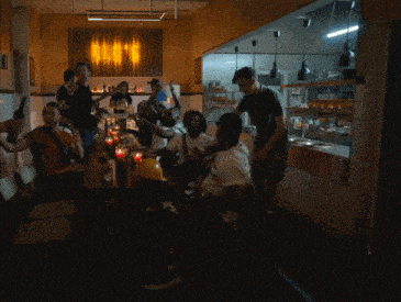 a group of people are gathered at a table in front of a sign that says ' bud 's ' on it