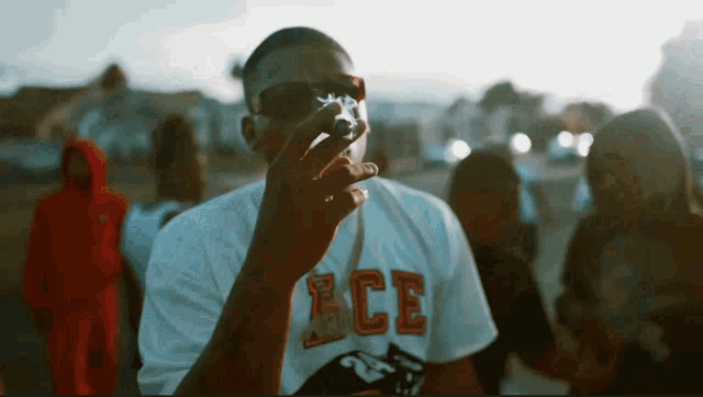 a man wearing a white shirt with the word ace on it smoking a cigarette