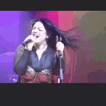 a woman singing into a microphone with her hair blowing in the air