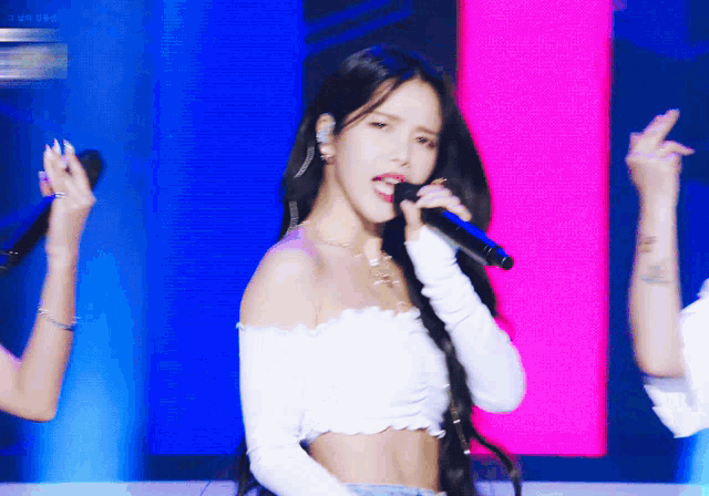 a woman singing into a microphone while wearing a white crop top