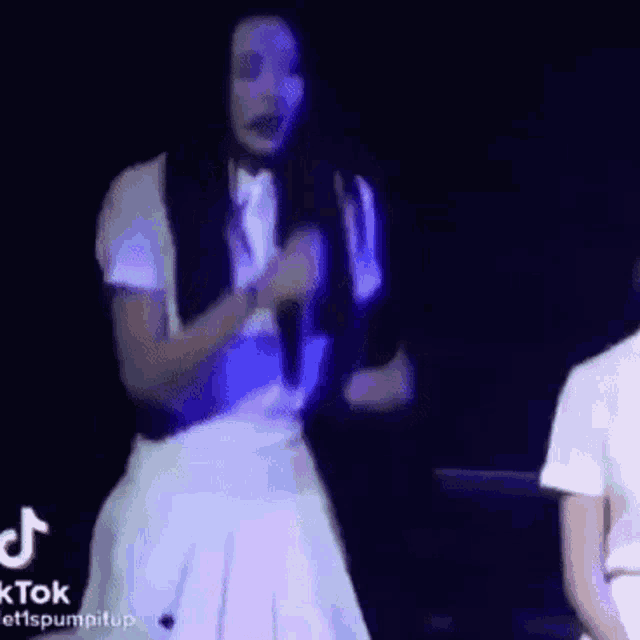 a woman in a white skirt is singing into a microphone while standing on a stage .