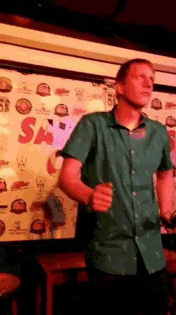 a man in a green shirt is dancing in front of a wall that has the word sa on it
