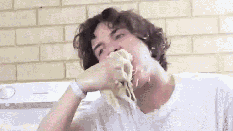 a man in a white shirt is eating a piece of food with his hand .