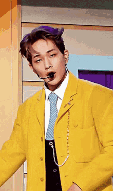 a man wearing a yellow jacket and a blue tie has a microphone in his mouth