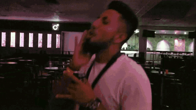 a man in a white shirt is talking on a cell phone in a dark room