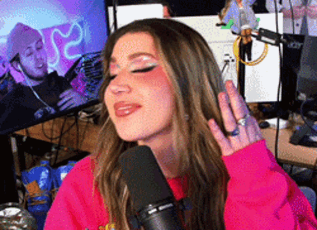 a woman is singing into a microphone while wearing a pink sweater