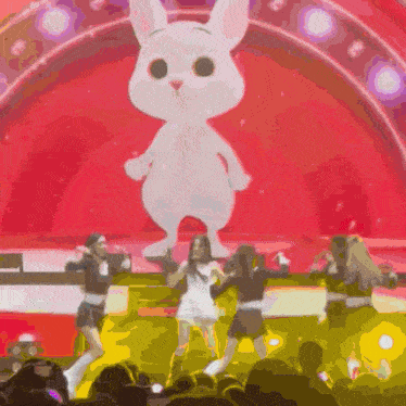 a group of women are dancing on a stage in front of a giant stuffed bunny