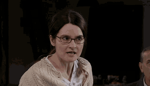 a woman wearing glasses and a sweater is looking at the camera