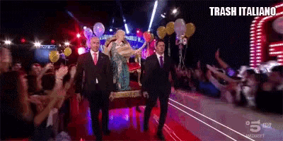 a statue of a woman is being carried on a red carpet in front of a crowd with the words trash italiano written above it