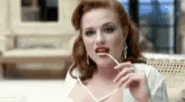 a woman with red hair is holding a pair of glasses in her mouth while sitting on a couch .