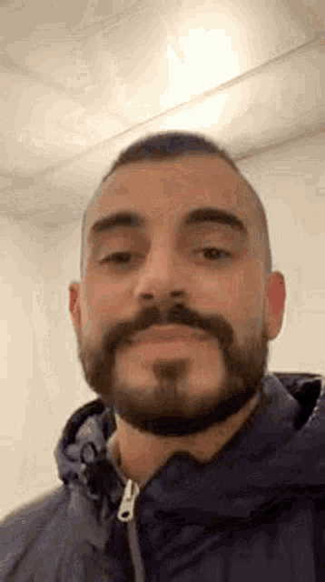 a man with a beard and mustache is wearing a blue jacket and making a face .